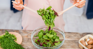 Salad green being tossed by person in a glass bowl