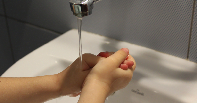 Water from tap running over child's hands.