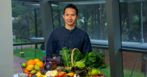Dr Marc Sim standing behind a bench with vegetables on it and windows in the background.