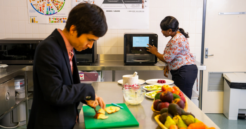 Dr Liezhou Zhong in foreground chopping apple, and Dr Dammy Adu in background 3D printing food
