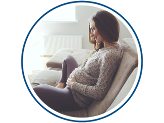 Pregnant woman sitting on a couch holding her belly.