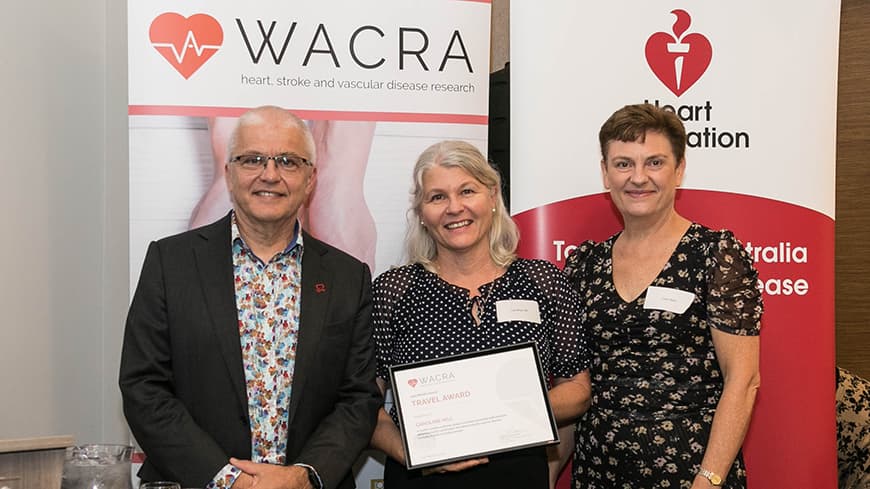 Dr Caroline Hill holds her framed award with two academics, WACRA pull-up banners are placed behind them.